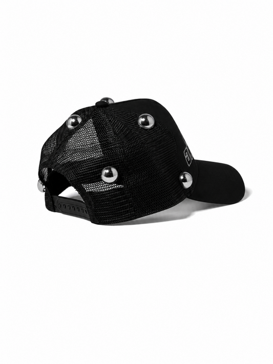 A black trucker-style cap with a mesh back and decorative silver metal studs on the front and brim, shown against a plain white background.
